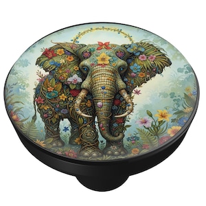 May include: A round, black phone grip featuring a detailed illustration of an elephant adorned with colorful flowers and foliage. The elephant has a golden halo and is set against a soft, floral background.
