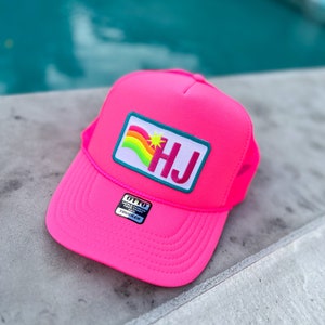 Puede incluir: Un gorro de camionero rosa con un parche de arcoíris y estrella que dice "HJ". El gorro tiene una etiqueta negra que dice "Otto World Famous For Front Of The Trucker"