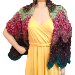 Puede incluir: Un chal de ganchillo multicolor con un degradado de rosa, verde, morado y turquesa. El chal está drapeado sobre un maniquí.