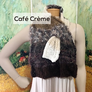 Puede incluir: Una bufanda de punto marrón y blanco con una textura esponjosa. La bufanda está atada en un nudo alrededor del cuello de un maniquí. La bufanda tiene un degradado de colores marrón, blanco y beige. El texto "Café Crème" está escrito en letras marrones sobre un fondo blanco.