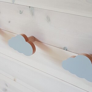 May include: Three wooden cloud-shaped hooks with a light gray finish mounted on a white wood wall.