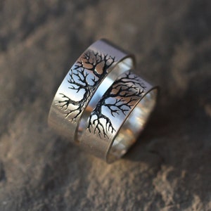 May include: Two silver rings with a tree design engraved on them. The rings are stacked on top of each other.