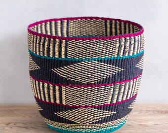 May include: A woven storage basket with a geometric pattern in black, white, teal, and pink. The basket is made of natural materials and has a cylindrical shape.
