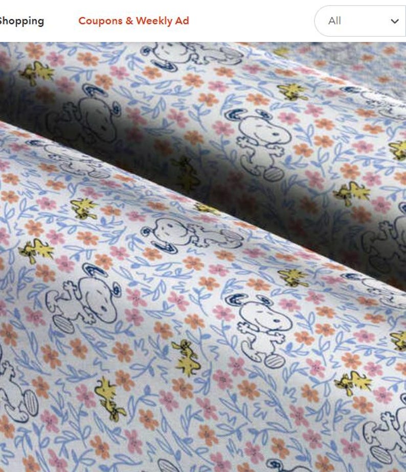 Puede incluir: Tela blanca con un patr&oacute;n repetido de Snoopy y Woodstock. Snoopy est&aacute; representado en un contorno azul y Woodstock es amarillo. El fondo es una tela blanca con un patr&oacute;n floral azul, rosa y naranja.