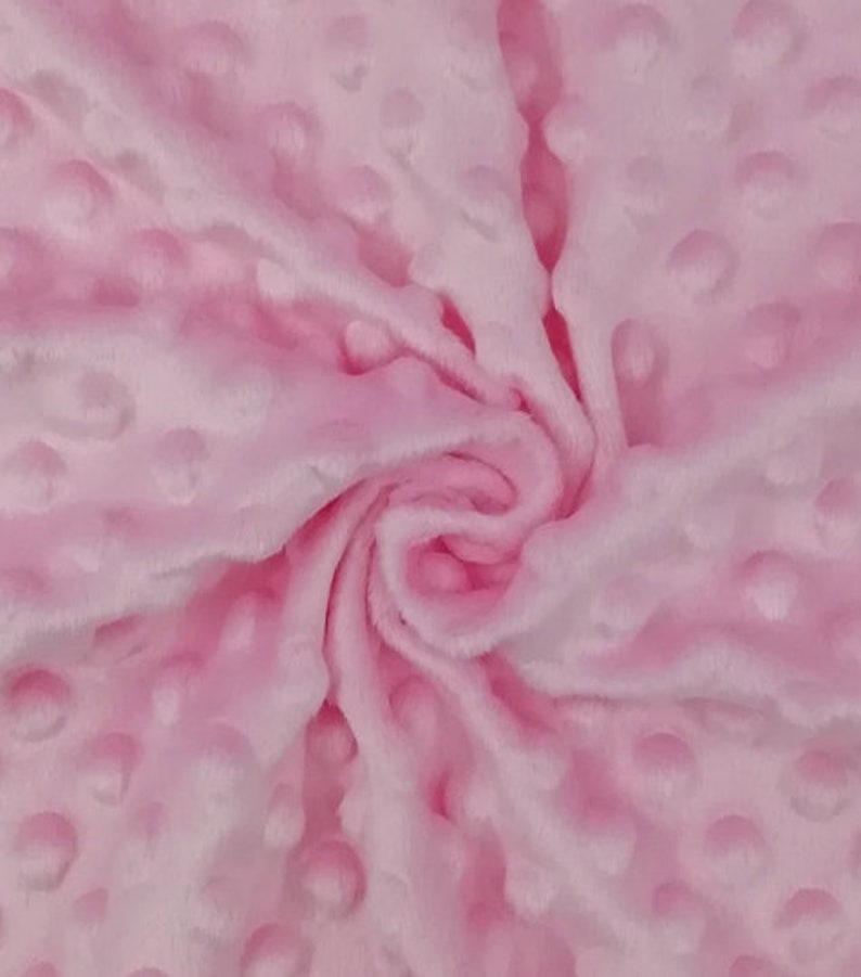 May include: Pink fabric with a textured, raised dot pattern. The fabric is soft and plush.