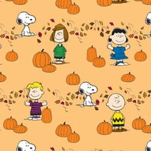 May include: A colorful fabric featuring the Peanuts characters, Snoopy, Charlie Brown, Lucy, and Linus, with pumpkins and autumn leaves on a light orange background.