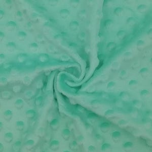 Puede incluir: Primer plano de una tela minky suave de color verde menta con un patr&oacute;n texturizado de puntos. La tela est&aacute; doblada y drapeada, mostrando su textura y color.