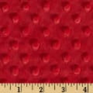 May include: Close-up of a red, textured fabric with a raised dot pattern. The fabric is shown with a ruler along the bottom, with measurements in inches. The fabric appears soft and plush.