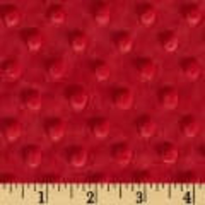 May include: Close-up of a red, textured fabric with a raised dot pattern. The fabric is shown with a ruler along the bottom, with measurements in inches. The fabric appears soft and plush.