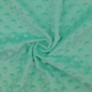 Puede incluir: Primer plano de una tela minky suave de color verde menta con un patr&oacute;n texturizado de puntos. La tela est&aacute; doblada y drapeada, mostrando su textura y color.