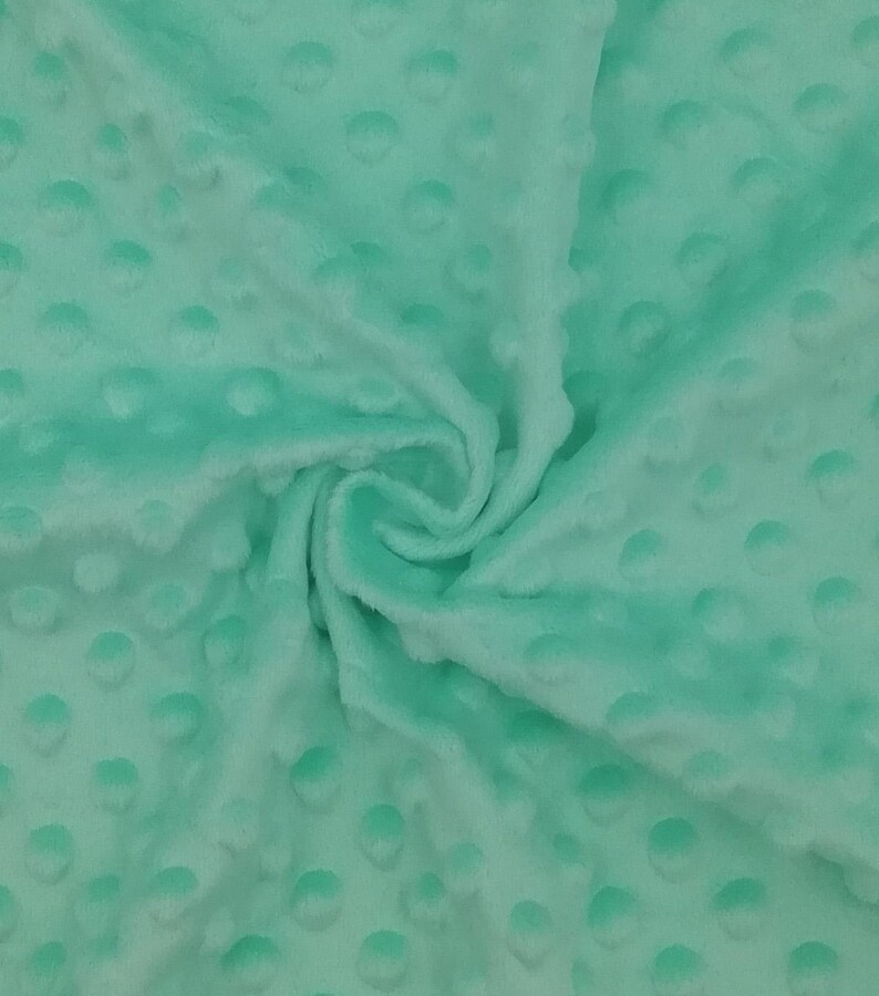 Puede incluir: Primer plano de una tela minky suave de color verde menta con un patr&oacute;n texturizado de puntos. La tela est&aacute; doblada y drapeada, mostrando su textura y color.