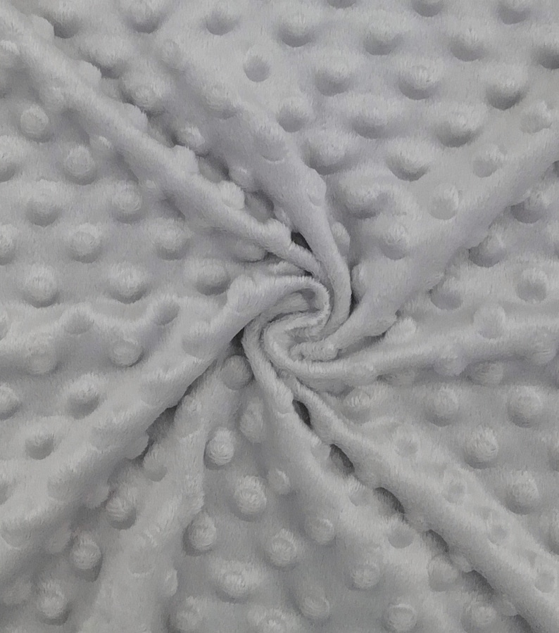 May include: Close-up of a soft, light gray fabric with a textured, dimpled surface. The fabric is folded and swirled, showing the plush texture and the raised, rounded dots that cover the material. The fabric appears to be a plush, cozy material.