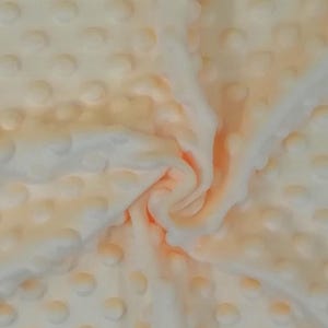 Puede incluir: Primer plano de una tela suave de color melocot&oacute;n con un patr&oacute;n texturizado de puntos en relieve. La tela est&aacute; doblada y drapeada, mostrando la textura y la variaci&oacute;n de color.