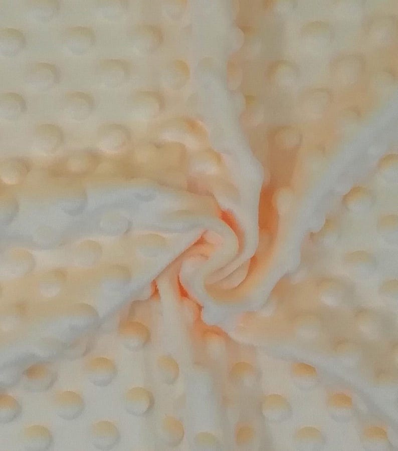 Puede incluir: Primer plano de una tela suave de color melocot&oacute;n con un patr&oacute;n texturizado de puntos en relieve. La tela est&aacute; doblada y drapeada, mostrando la textura y la variaci&oacute;n de color.
