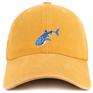 Puede incluir: Gorra de béisbol de color amarillo mostaza con un diseño bordado de tiburón ballena azul y blanco. La gorra tiene una visera curva y una correa ajustable. El diseño del tiburón ballena presenta puntos blancos.