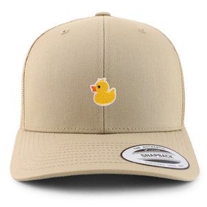 May include: A tan and black mesh trucker hat with a yellow rubber ducky embroidered on the front. The hat has a black mesh back and a tan front panel. The hat has a black adjustable strap with a plastic buckle. The hat has a white label on the back that says "The Authentic Yupoong Snapback Yupoong Since 1974."