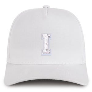 May include: White baseball cap with a sequined letter "I" patch. The letter is in a light pink and white color scheme. The cap has a curved brim and a button on top.