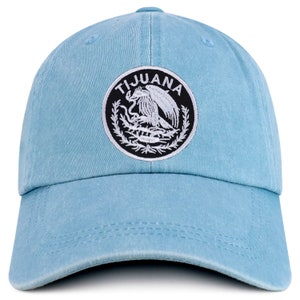 May include: A light blue baseball cap with a black and white embroidered patch that says "TIJUANA" and features a stylized eagle.