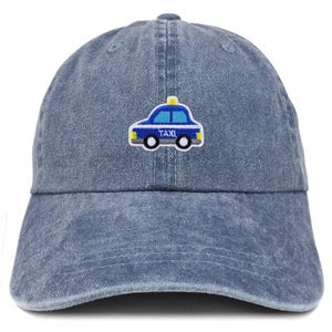 May include: A blue denim baseball cap with a curved brim. The cap features an embroidered taxi cab design in blue, white, yellow, and black. The word "TAXI" is embroidered on the side of the car.