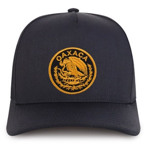 May include: Black baseball cap with a gold embroidered emblem featuring a stylized eagle and the word "OAXACA".