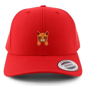 May include: A red trucker hat with a mesh back and a cat face embroidered on the front. The cat is orange and white with large eyes. The hat has a curved brim and a snapback closure.