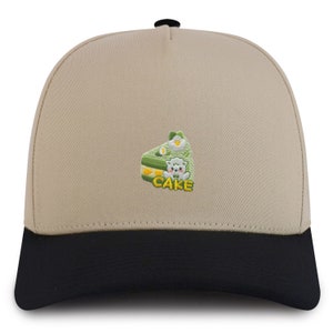 May include: A beige and black baseball cap with an embroidered green cake slice with a white sheep and the word "CAKE" in yellow.