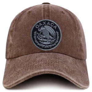 May include: A brown baseball cap with a gray embroidered patch featuring the text "OAXACA" and a stylized eagle design.