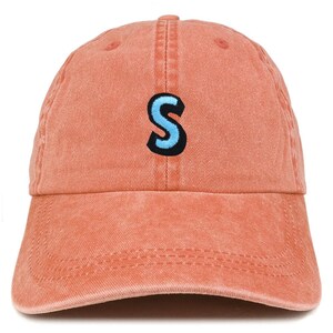 May include: A coral-colored baseball cap with a curved brim. The cap features a light blue letter "S" with a black outline embroidered on the front. The hat is made of a soft, textured fabric.
