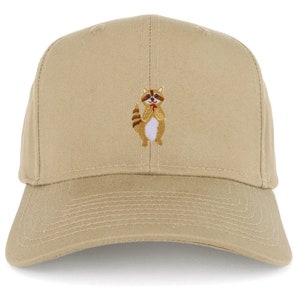 May include: A beige baseball cap with an embroidered raccoon holding a red heart. The raccoon is brown, white, and black.