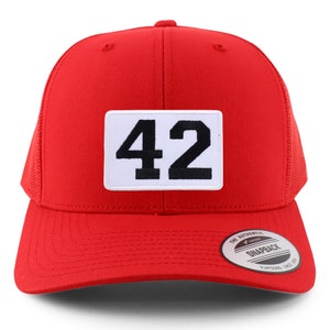 Puede incluir: Gorra de camionero roja de malla con un parche blanco que muestra el número 42 en negro. La gorra tiene un cierre de presión negro y una etiqueta blanca con el texto "The Authentic Snapback Yupoong Since 1974".