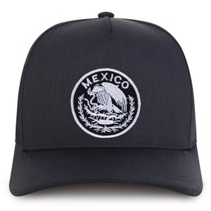 Peut inclure: Casquette de baseball noire avec un cercle brodé blanc représentant les armoiries mexicaines et le mot "MEXICO" au-dessus.