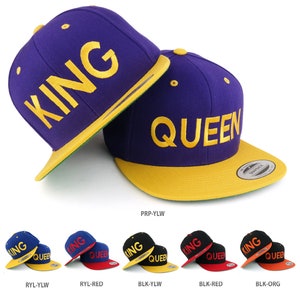 Puede incluir: Dos gorras de béisbol, una morada con visera amarilla y la palabra "KING" bordada en amarillo, la otra morada con visera amarilla y la palabra "QUEEN" bordada en amarillo.
