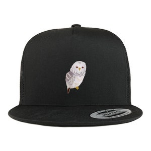 Op de afbeelding: Een zwarte truckercap met een witte uil geborduurd op de voorkant. De pet heeft een zwart mesh achterkant en een zwarte drukknopsluiting.