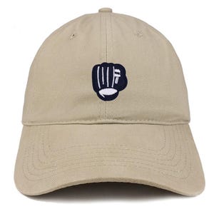 May include: A beige baseball cap with a curved peak. The cap has a navy blue embroidered fist design on the front. The cap is made of a soft fabric and has an adjustable fit.