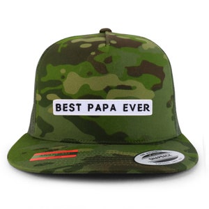 Op de afbeelding: Een groene camouflage trucker cap met een wit patch waarop in zwarte letters "BEST PAPA EVER" staat.