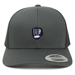 May include: A dark grey snapback baseball cap with a mesh back. The cap features a navy blue and white embroidered fist logo. The brim is curved, and the cap has a snap closure. The tag on the front of the cap reads "THE CLASSICS SNAPBACK".