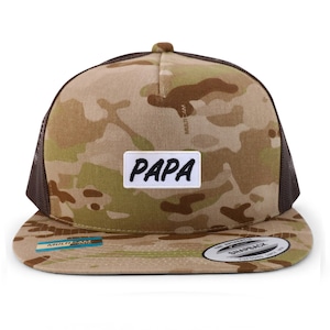 Puede incluir: Una gorra de camionero de camuflaje marrón y beige con una malla negra en la parte posterior. La gorra tiene un parche blanco con la palabra "PAPA" escrita en negro.