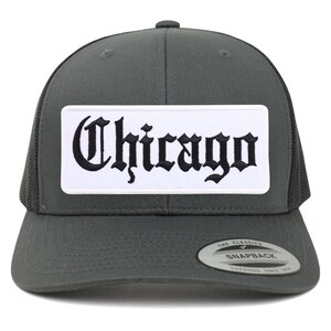 Puede incluir: Una gorra de camionero gris oscuro con un parche blanco que dice "Chicago" en letras góticas negras. La gorra tiene una parte trasera de malla negra y un cierre de presión negro.