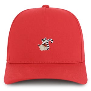 Könnte beinhalten: Eine leuchtend rote Baseballkappe mit einem gestickten Lemuren-Design. Der Lemur hat ein weißes, schwarzes und braunes Farbschema. Die Kappe hat einen gebogenen Schirm und einen Knopf oben.