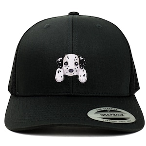 May include: Black trucker hat with a white and black dalmatian puppy peeking out from behind the front panel. The hat has a black mesh back and a black snap closure. The hat has a sticker on the back that says "The Classics" and "Snapback" with the Yupoong logo.