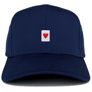 Könnte beinhalten: Marineblaue Baseballkappe mit einem kleinen weißen quadratischen Aufnäher mit einem roten Herz. Die Kappe hat einen gebogenen Schirm und eine strukturierte Krone. Klassisches Design.