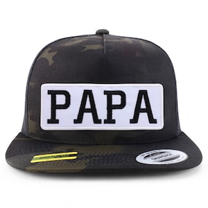 May include: A black and green camouflage trucker hat with a white patch that says "PAPA" in black letters.
