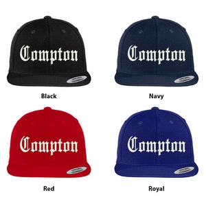 May include: Four baseball caps in different colors: black, navy, red, and royal blue. Each cap features the word "Compton" in white, stylized lettering.