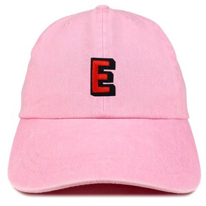 May include: A light pink baseball cap with a curved brim. The cap features an embroidered letter "E" in red with a black outline on the front. The cap is made of a soft fabric.