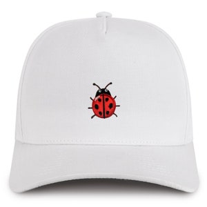 Könnte beinhalten: Weiße Baseballkappe mit einer roten Marienkäfer-Stickerei auf der Vorderseite.
