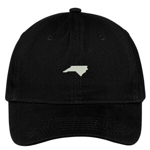 Puede incluir: Una gorra de b&eacute;isbol negra con un contorno blanco del estado de Carolina del Norte en la parte delantera.