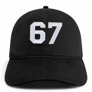 May include: Black baseball cap with the number 67 embroidered in white on the front. The cap has a curved brim and a button on top. This hat is a classic accessory.