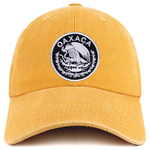 May include: A yellow baseball cap with a black and white embroidered patch featuring the Coat of Arms of Mexico and the word "OAXACA".