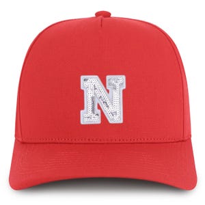 May include: A bright red baseball cap featuring a large, sequined letter "N" in silver and white. The cap has a curved brim and a structured crown, suitable for casual wear and sports events.