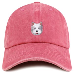 May include: A dusty rose baseball cap with a curved brim. The cap features an embroidered image of a white and gray dog's face on the front. The cap is made of a soft, textured fabric.